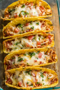 Freshly baked tacos showing layers of chicken, lettuce, and melted cheese against a rustic backdrop.