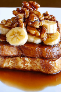 Close-up of caramelized bananas and walnuts resting on buttery toast with syrup pooling around the edges.