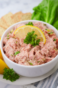 Rustic presentation of a savory spread in a white bowl, paired with lemon slice and herbs.
