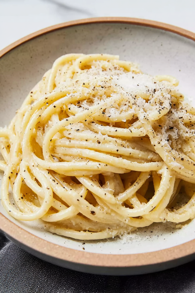 Rustic ceramic bowl filled with glossy noodles finished with parmesan and pepper