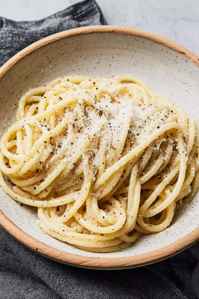 Homemade bucatini cacio e pepe served warm with a generous layer of grated cheese