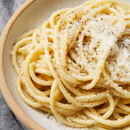 Close-up of bucatini pasta coated in creamy cheese sauce with cracked black pepper