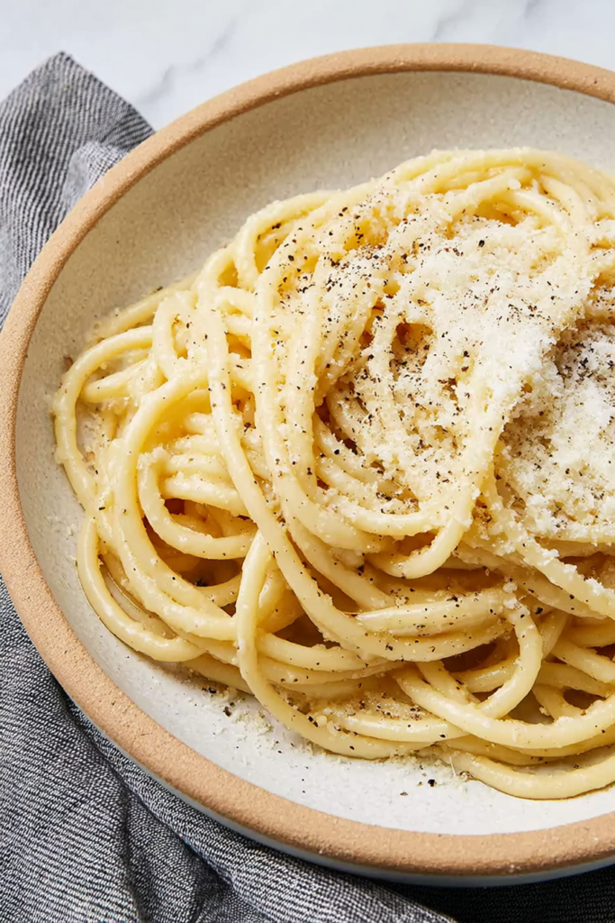 Close-up of bucatini pasta coated in creamy cheese sauce with cracked black pepper