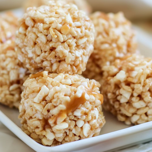 Close-up of caramel-coated Rice Krispie balls stacked on a white plate with a soft drizzle of melted marshmallow.
