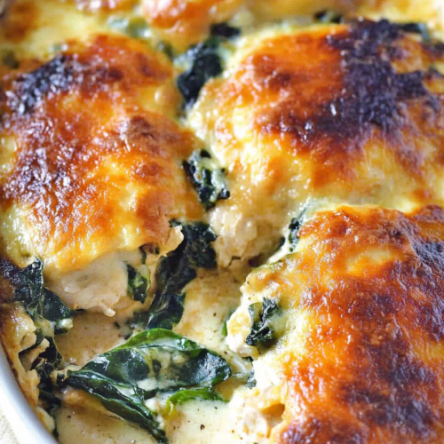 Chicken casserole with spinach topped with golden, bubbly melted cheese in a white baking dish.