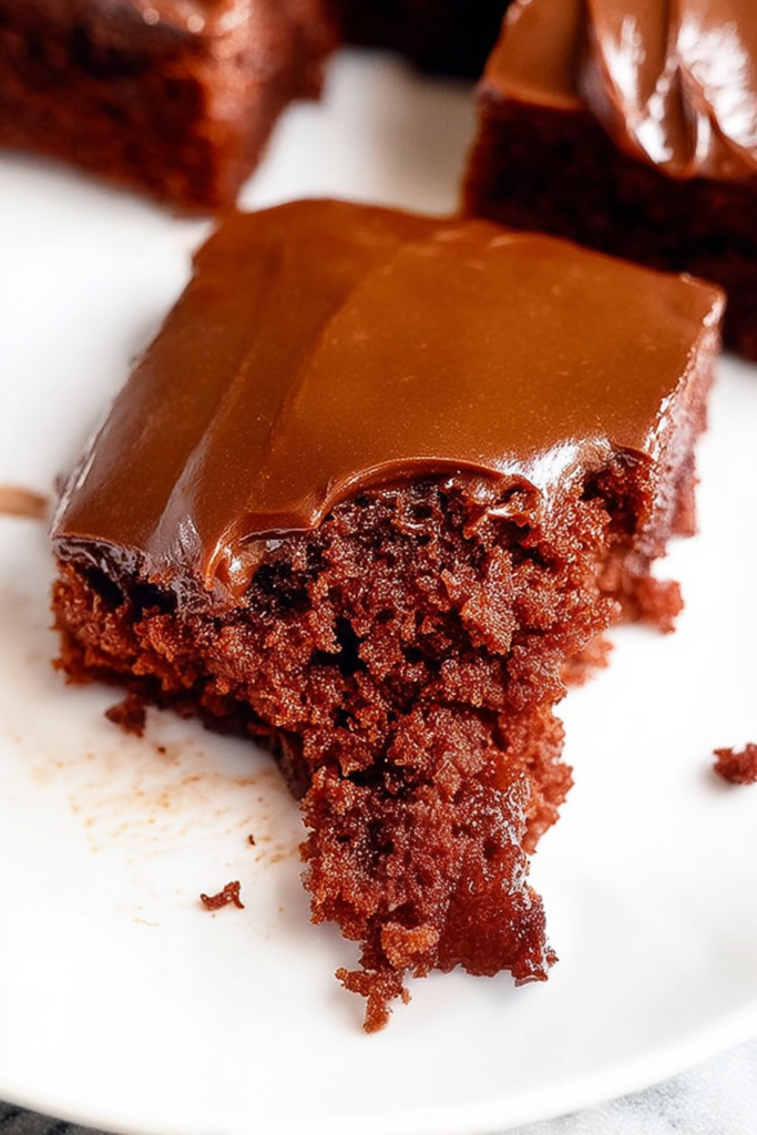 Moist chocolate cake square topped with smooth, glossy frosting.