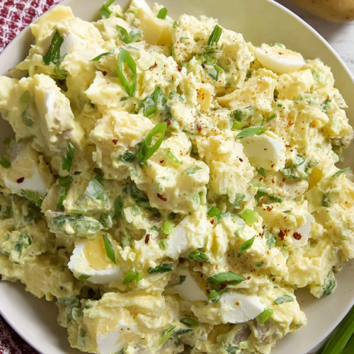 Close-up of creamy potato and egg salad with herbs and seasoning.