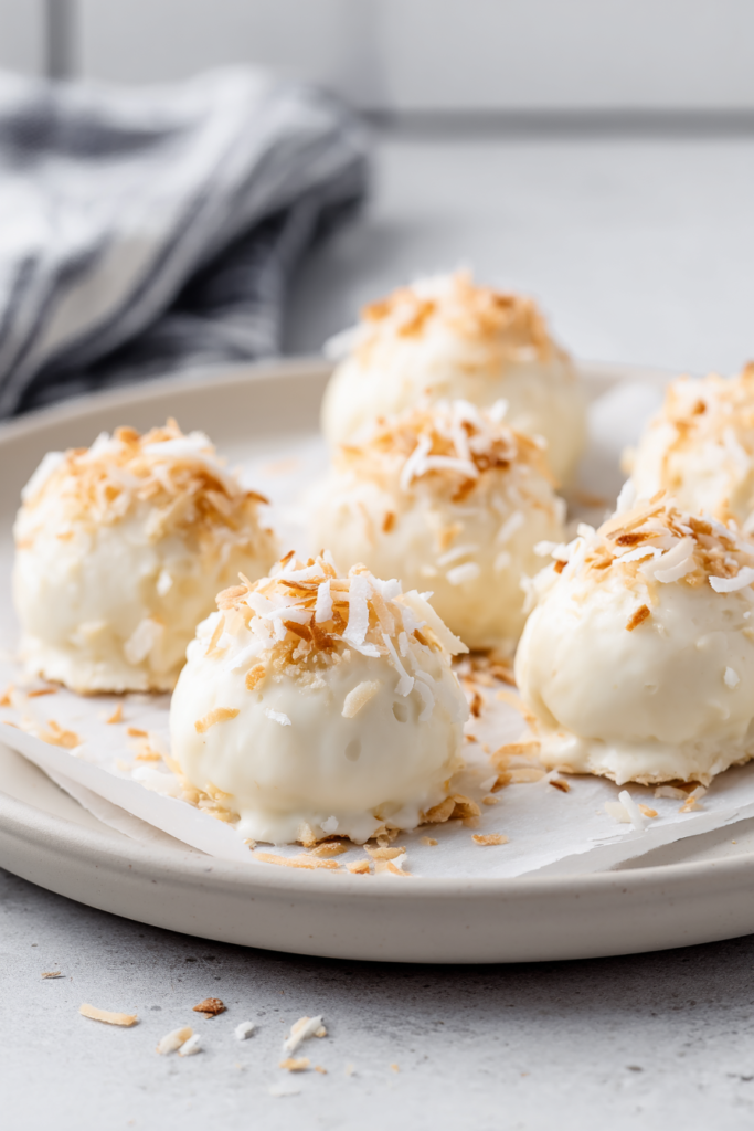 Creamy white chocolate truffles topped with toasted coconut flakes on a serving plate
