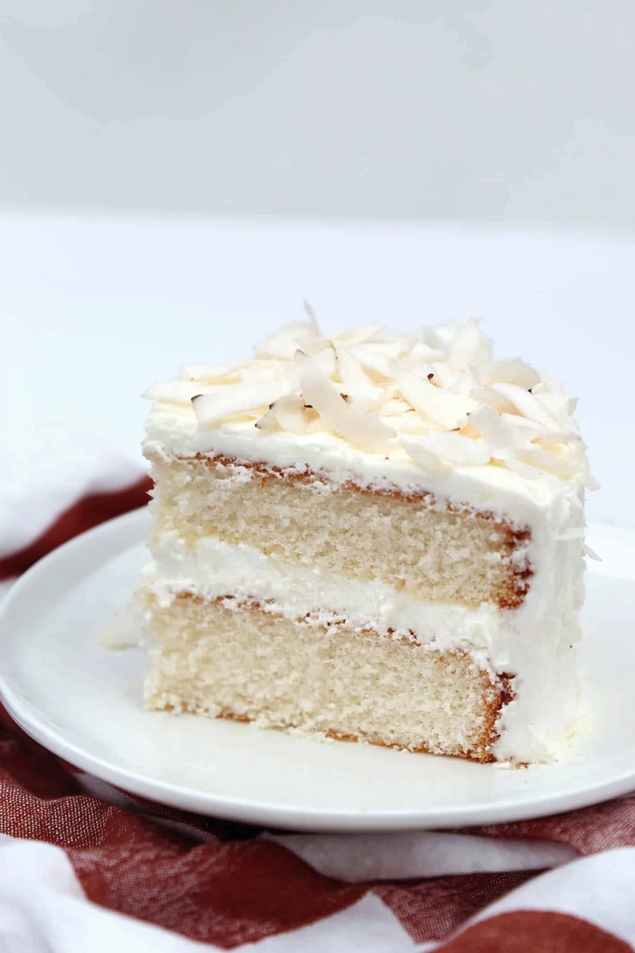 Close-up of a moist vanilla cake slice showing creamy filling and coconut garnish on top.