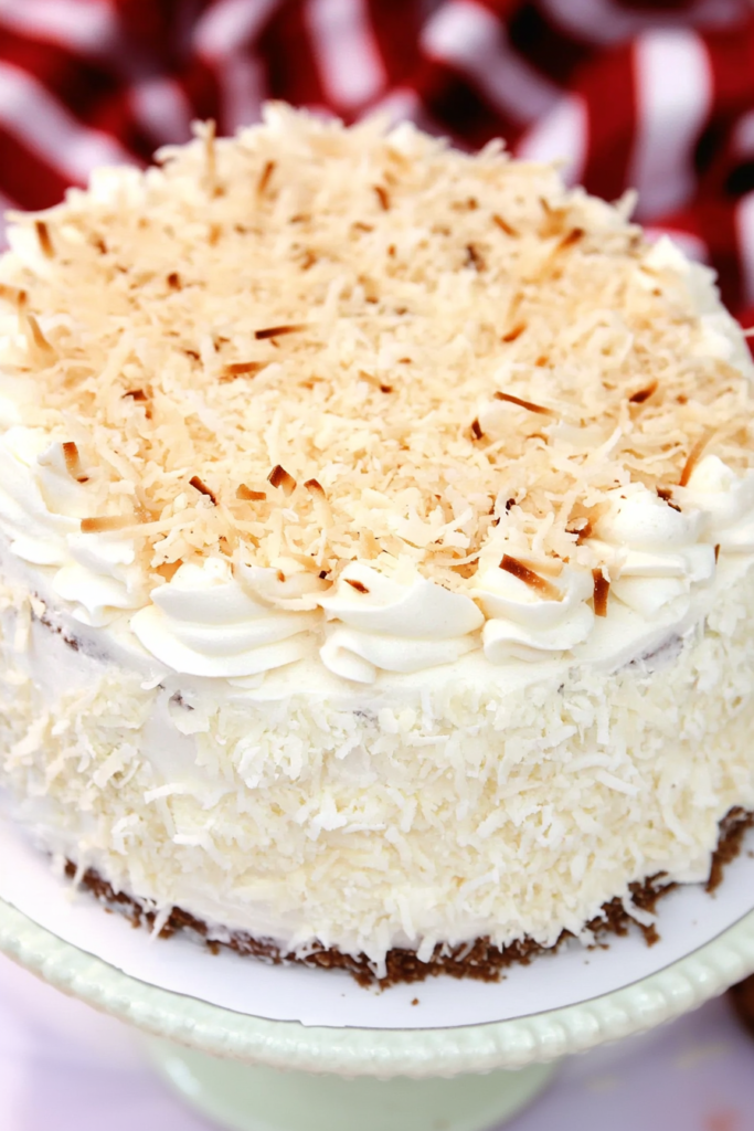 Whole layered cake with smooth white frosting and golden coconut shreds, styled for a celebratory table setting.