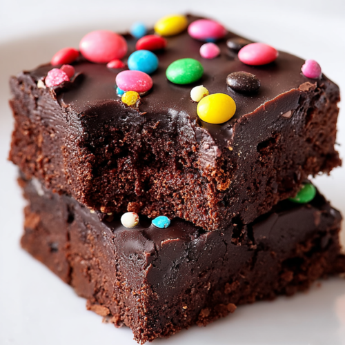 Close-up of moist, dense brownies with glossy frosting and vibrant candy pieces scattered on top.