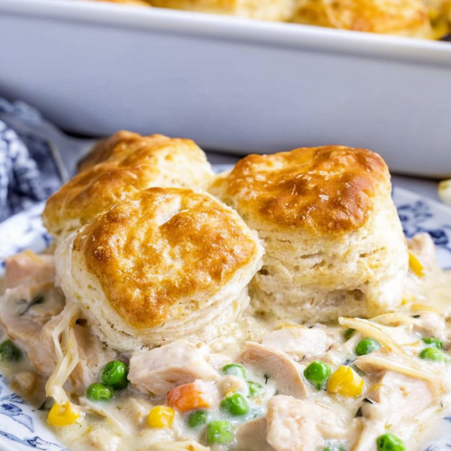 Golden baked biscuits served over creamy chicken with peas and vegetables on a plate.