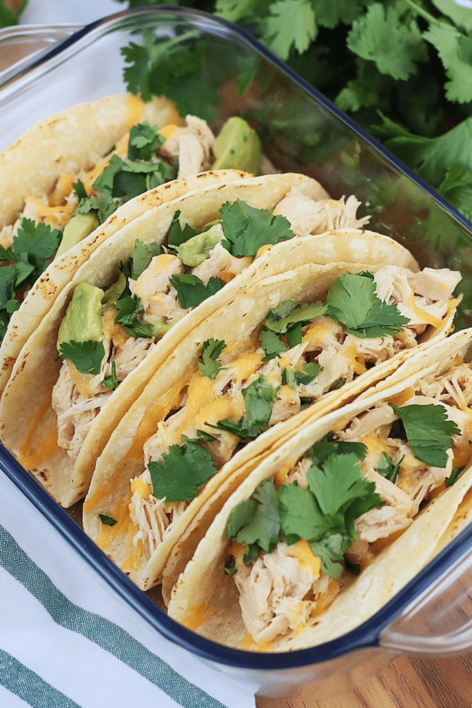 Cheesy chicken tacos arranged on a checkered cloth with fresh cilantro sprigs nearby.