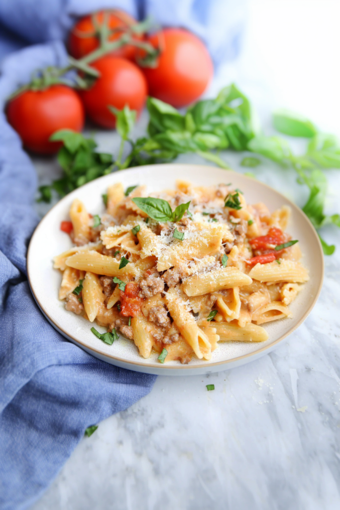 Creamy sausage pasta with tomatoes served warm on a plate.
