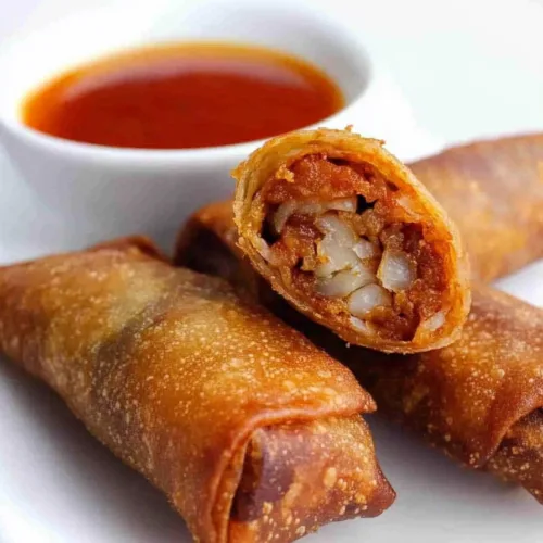 Plate of crispy appetizer rolls with bubbling golden texture and sweet dipping sauce in the background.