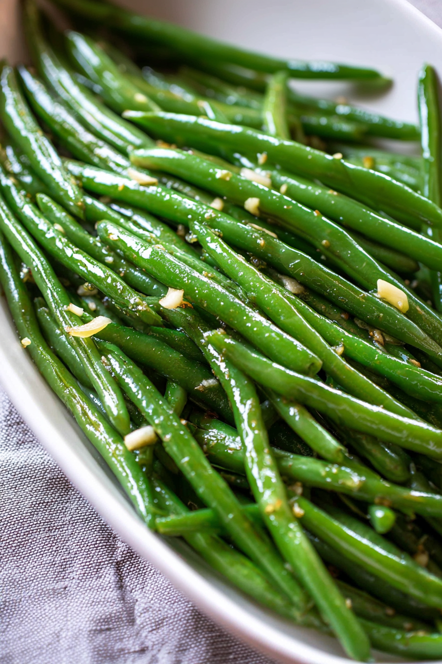 Fresh green beans served on a white platter with bits of minced garlic.