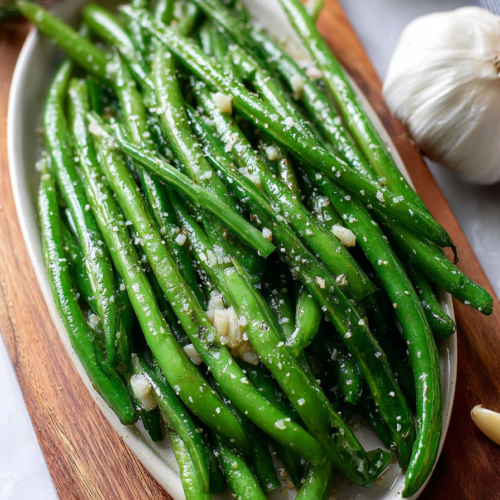 Simple side dish of glossy green beans garnished with sea salt and herbs.