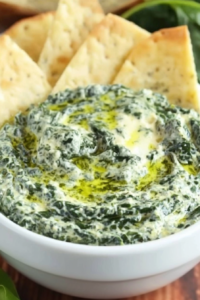 Close-up of rich green and white dip with a marbled texture, styled with fresh spinach leaves nearby.