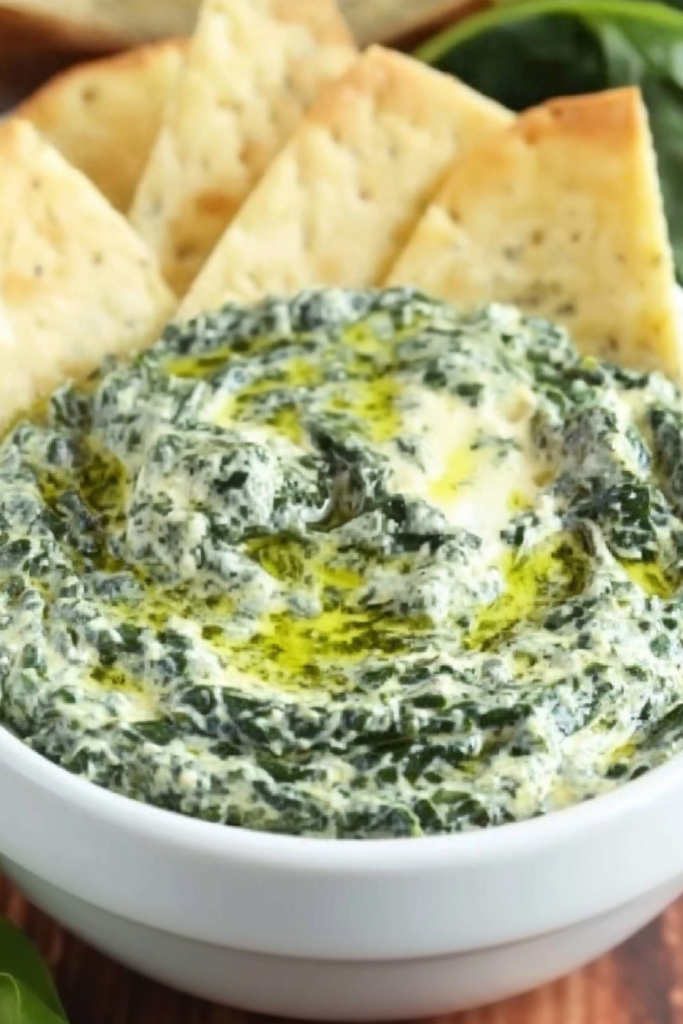 Close-up of rich green and white dip with a marbled texture, styled with fresh spinach leaves nearby.