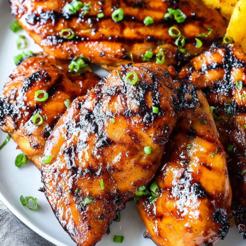 Close-up of barbecue chicken pieces brushed with honey glaze and paired with grilled pineapple rings.