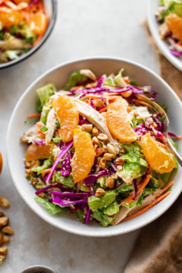 Fresh green salad topped with grilled chicken, juicy mandarin slices, red cabbage, and chopped nuts.