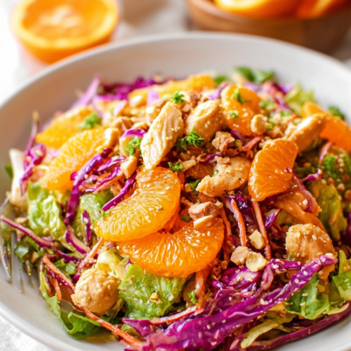 Close-up of a hearty salad featuring sliced chicken, fresh lettuce, citrus fruit, and nutty topping.