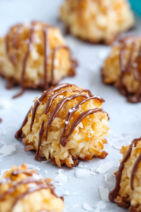Close-up of chewy coconut dessert bites topped with a glossy chocolate drizzle.