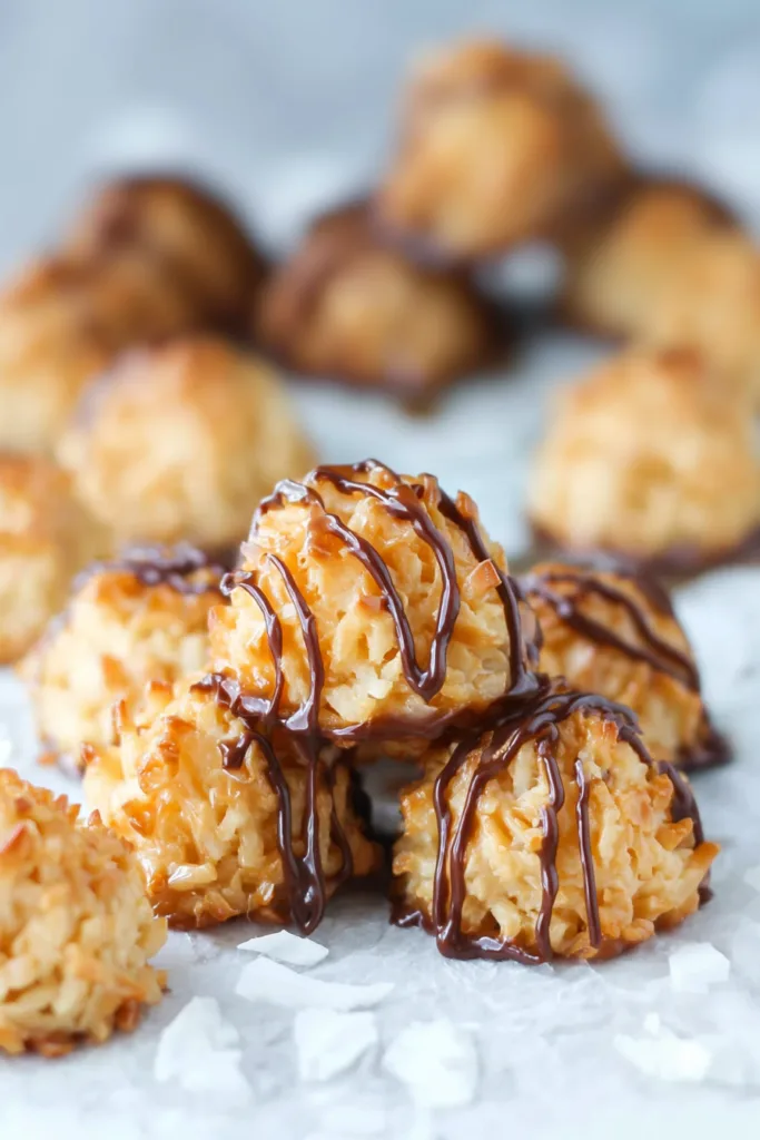 Golden coconut macaroons drizzled with chocolate and caramel, stacked on parchment paper.