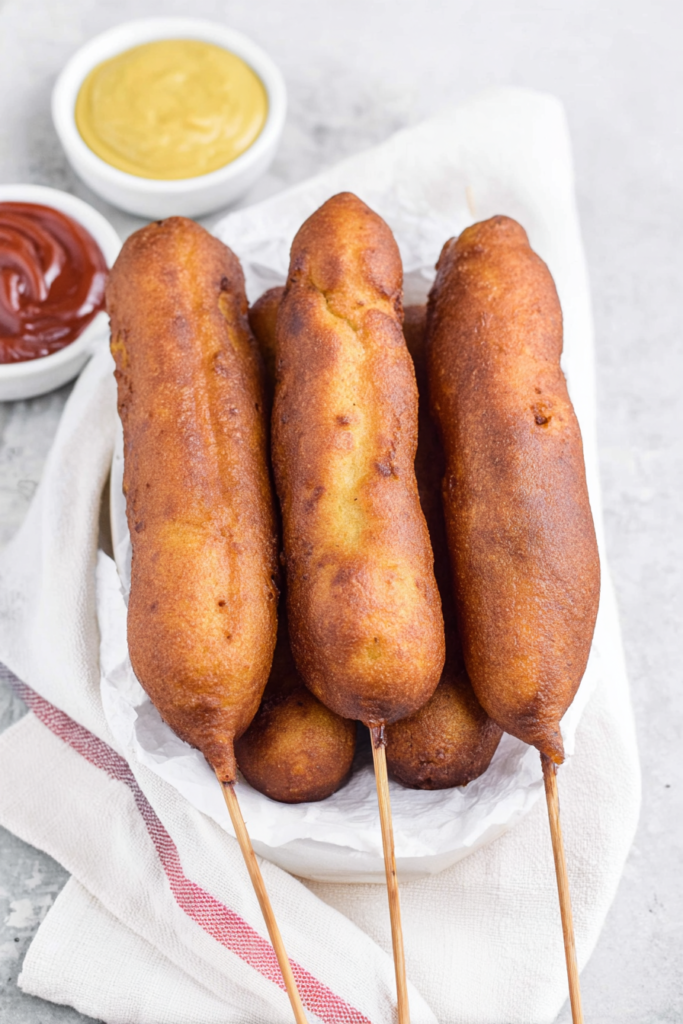 Final serving of corn dogs with a crisp coating, paired with a bright yellow sauce for dipping.