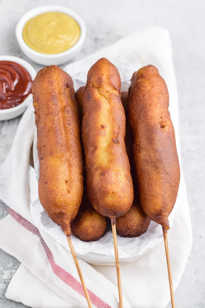 Final serving of corn dogs with a crisp coating, paired with a bright yellow sauce for dipping.