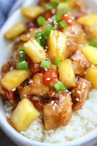 Close-up of tender chicken and pineapple chunks garnished with scallions and sesame seeds.