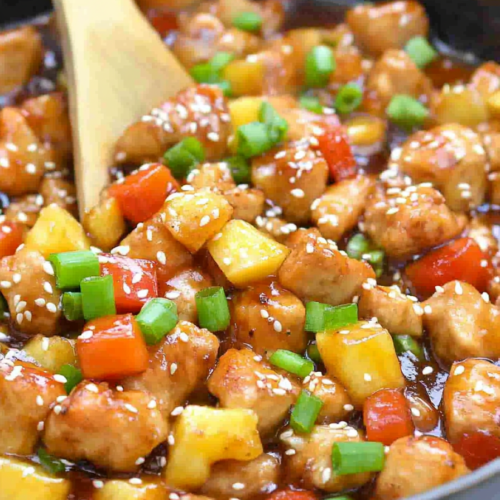 Bowl of glazed chicken with fresh pineapple, red bell peppers, and sesame seeds on top.