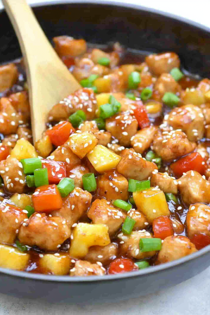 Bowl of glazed chicken with fresh pineapple, red bell peppers, and sesame seeds on top.