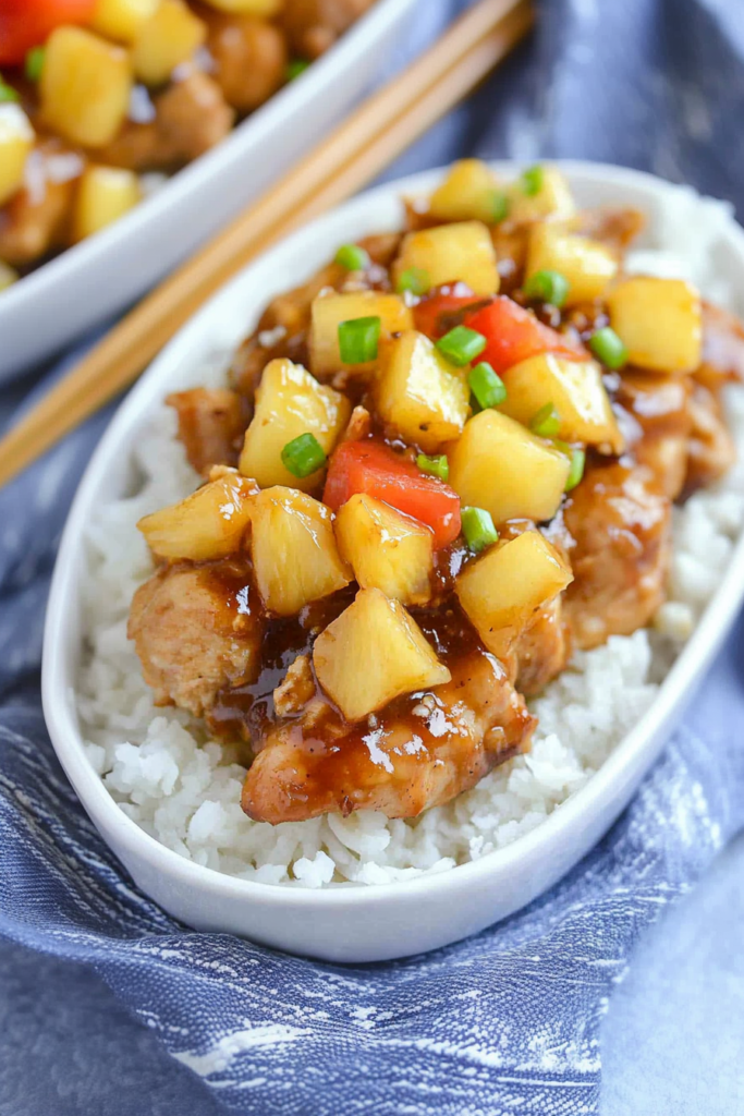Saucy chicken and pineapple served in a bowl with fluffy rice and colorful vegetables.