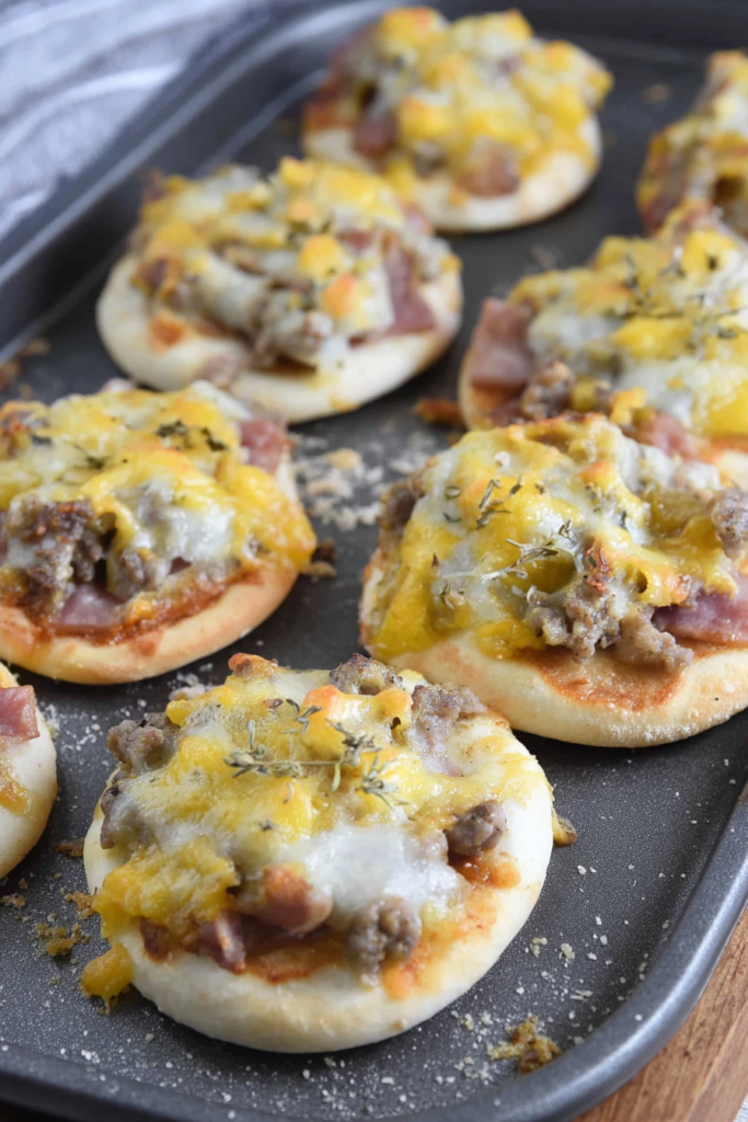 Mini pizza topped with melted cheese, sausage, and scrambled eggs on a baking tray.