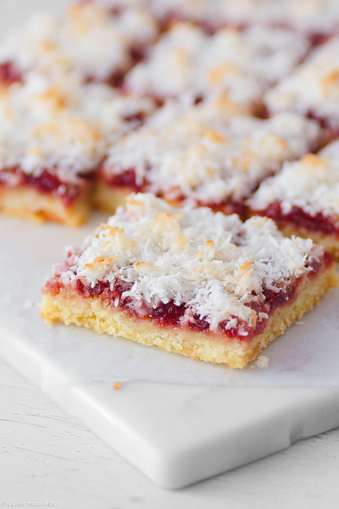 Plated slice highlighting the contrast between buttery base, ruby-red filling, and snowy coconut layer.