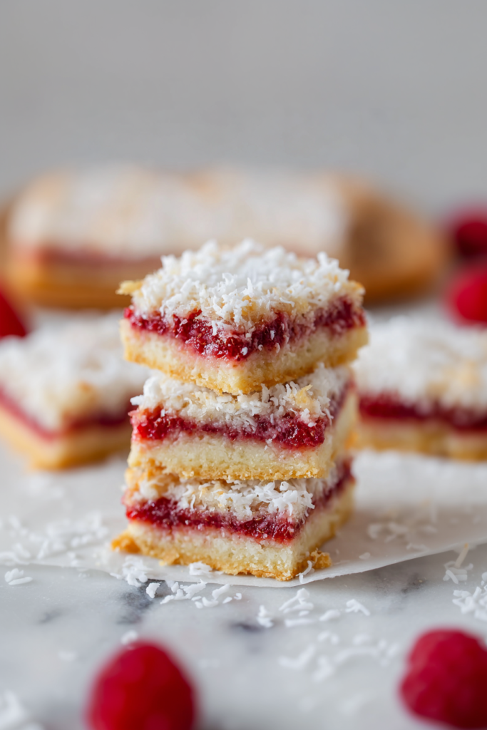 Three neatly cut squares with visible raspberry layer and coconut finish, placed on a white surface.