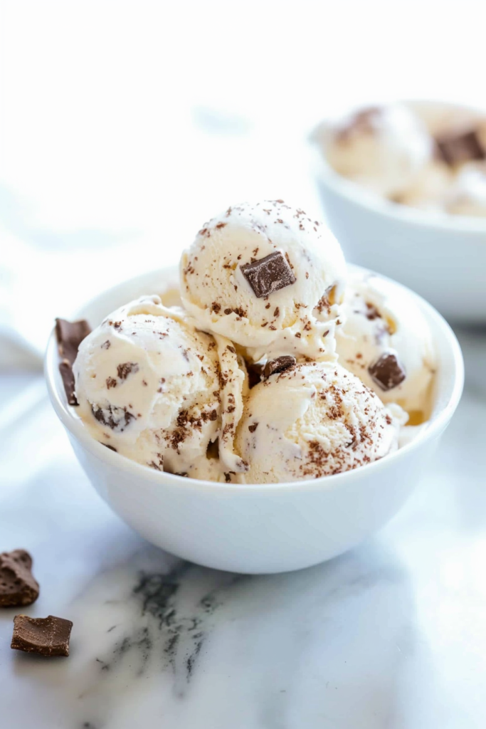 Scoops of creamy ice cream in a bowl, with visible chocolate chunks and a rich texture.