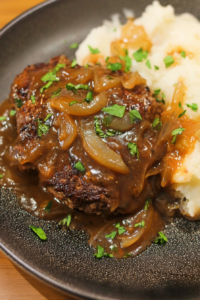 Homemade beef patty covered in rich brown gravy and caramelized onions, plated with mashed potatoes.