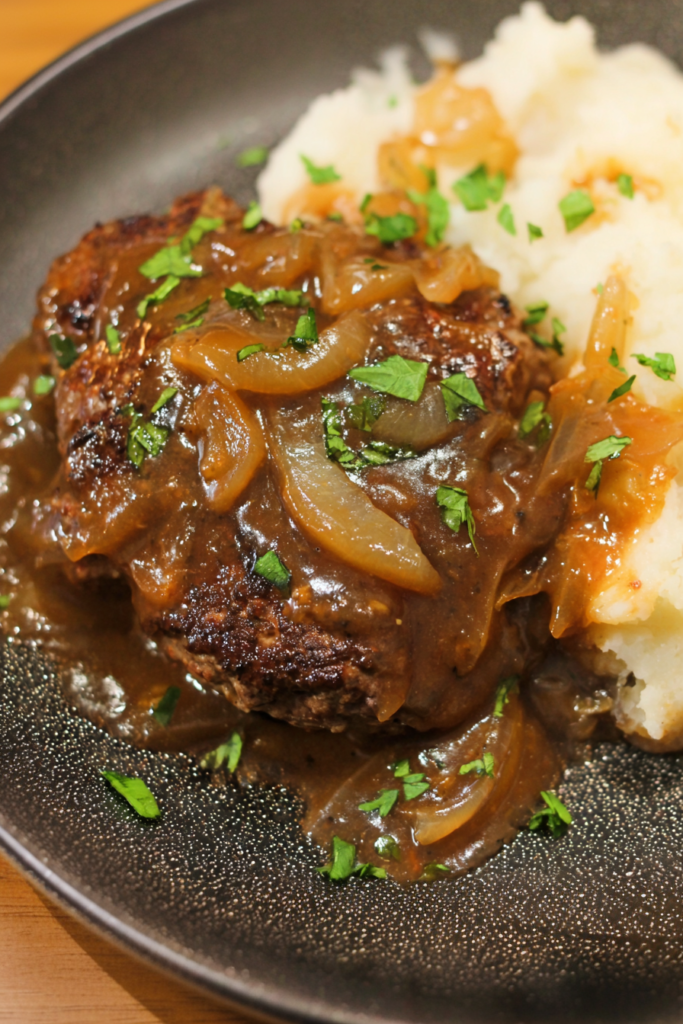Homemade beef patty covered in rich brown gravy and caramelized onions, plated with mashed potatoes.
