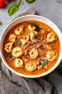 Close-up of tortellini floating in rich tomato soup topped with grated cheese
