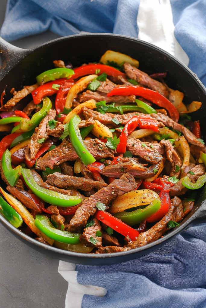 Skillet filled with sizzling strips of beef, peppers, and onions.