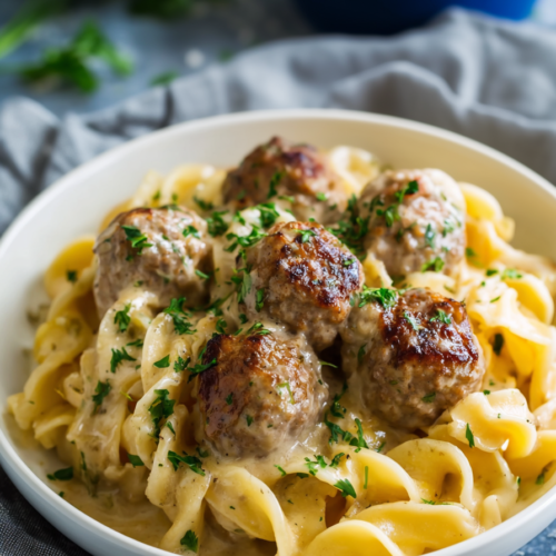 Bowl of creamy egg noodles topped with browned meatballs and sprinkled parsley.