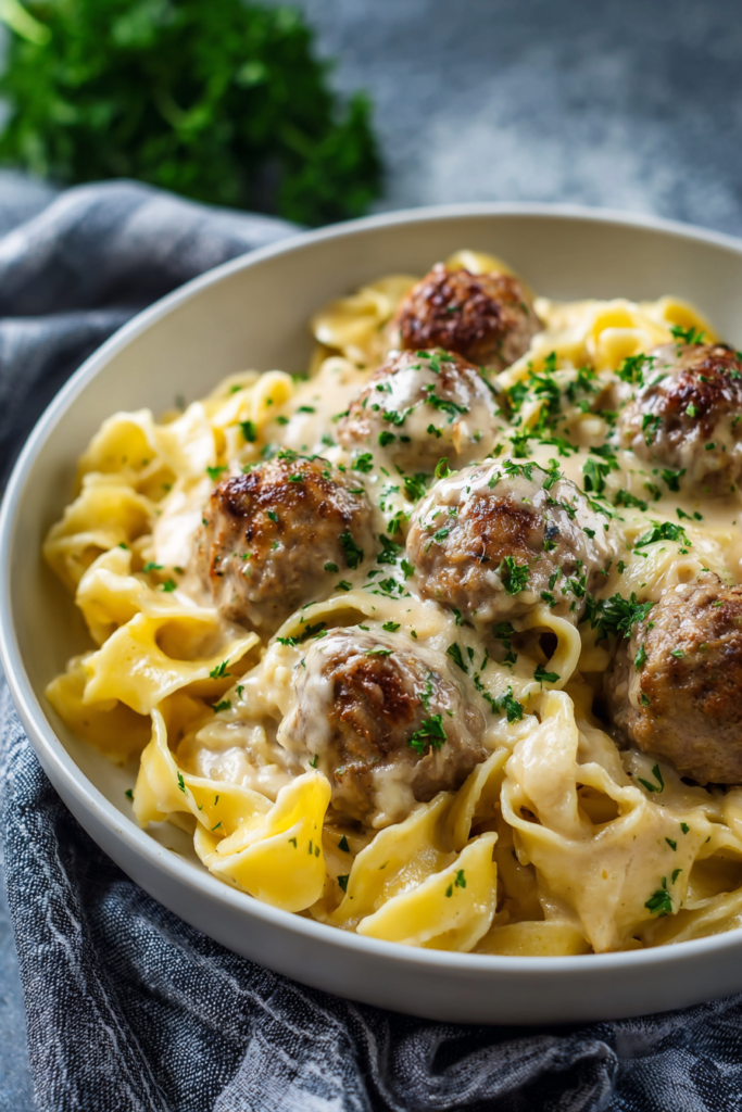Hearty pasta bake featuring glossy noodles and browned meatballs, accented with chopped parsley.