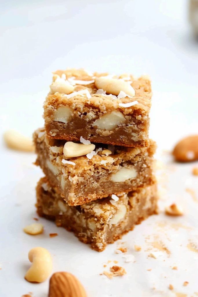 Stack of white chocolate coconut blondies topped with sliced almonds and shredded coconut.