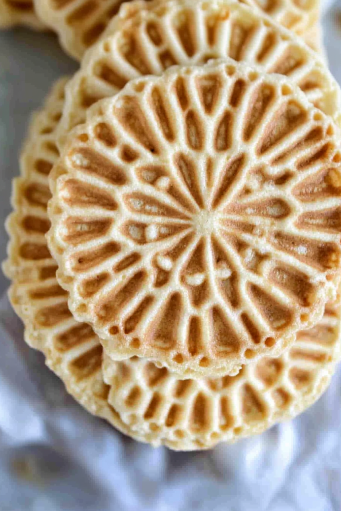 Stack of thin, golden pizzelle cookies with intricate floral patterns.