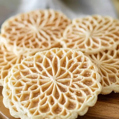 Freshly made pizzelle stacked together, showcasing their lacy surface and crisp edges.