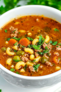 Warm, rustic soup filled with pasta, carrots, peppers, and beef, topped with chopped parsley.
