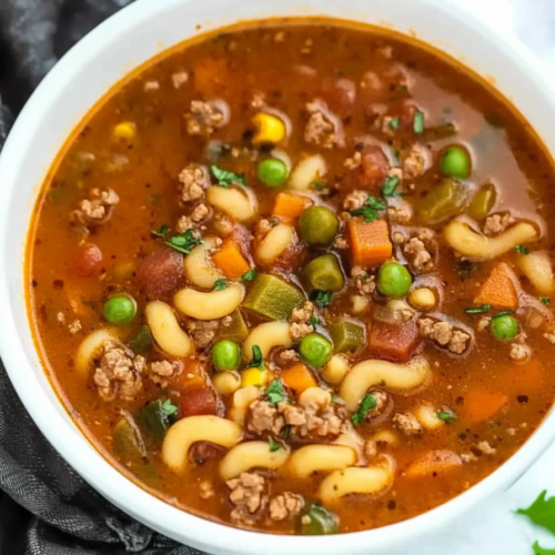 Rich, comforting soup with elbow macaroni, ground meat, and colorful vegetables in a tomato broth.