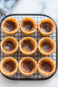 Freshly baked tarts cooling on a wire rack, with golden crusts and glossy caramelized filling.